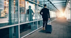 Businessman walking outside public transport building with luggage